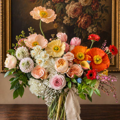 Mixed pastel bouquet with poppies, roses, tulips, and gerbera daisies in a glass vase