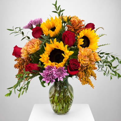 Bouquet of sunflowers, red roses, and purple mums in a glass vase
