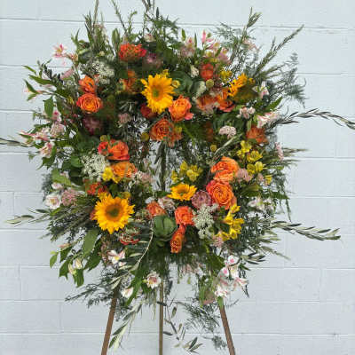 Large floral wreath on a stand with orange roses and yellow sunflowers