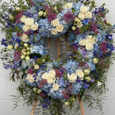 Large floral wreath of blue hydrangeas, white roses, and purple flowers on an easel