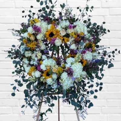 Large floral wreath on an easel with white, yellow, and purple flowers
