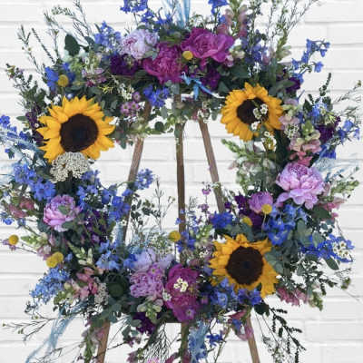Large floral wreath with sunflowers, purple blooms, and blue flowers on a stand