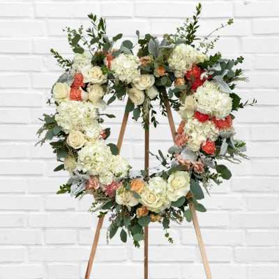 Heart-shaped floral wreath on a wooden stand with white and peach flowers