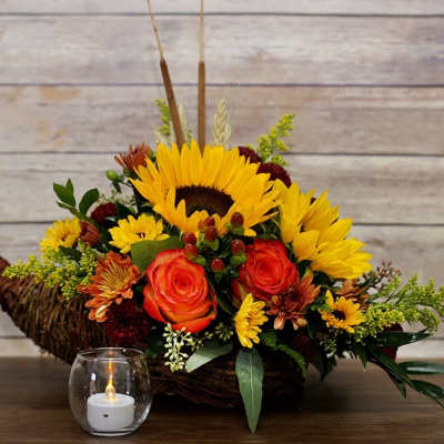 Sunflower and rose arrangement in a wicker basket with a small candle in front