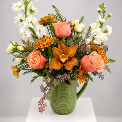 Peach roses and orange blooms in a green ceramic pitcher