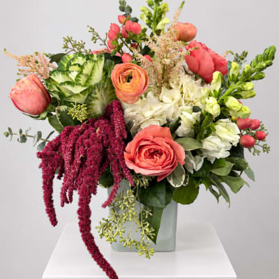 Mixed bouquet with coral roses, white blooms, and green snapdragons in a glass vase
