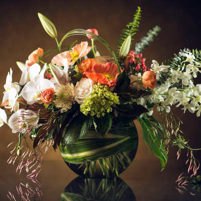 Mixed floral arrangement in a round glass vase with white orchids and orange poppies