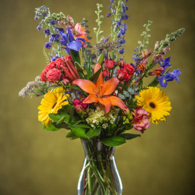 Mixed bouquet in a clear glass vase with orange lilies and yellow daisies