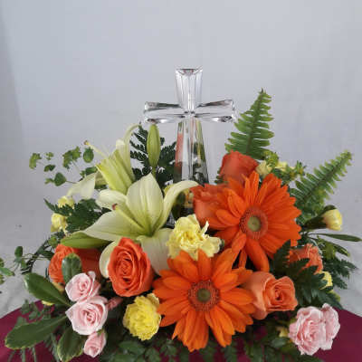 Floral arrangement with a clear glass cross and orange, white, and pink flowers