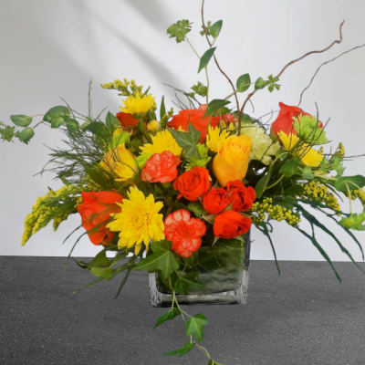 Mixed bouquet of yellow and orange flowers in a square glass vase