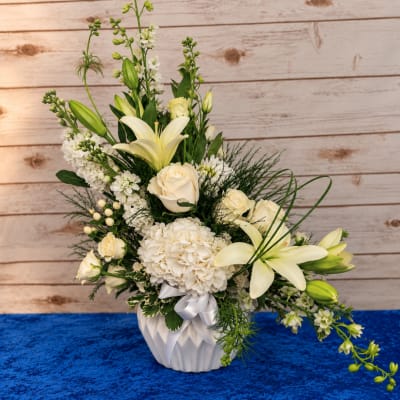 White floral arrangement in a white vase with lilies and roses