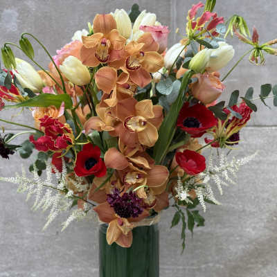 Mixed bouquet with orange orchids, red anemones, and pale tulips in a green vase
