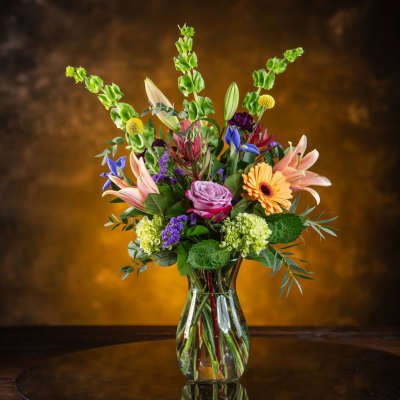 Mixed bouquet in a clear glass vase with lilies, roses, and gerbera daisies