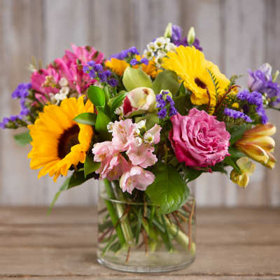 Mixed bouquet with sunflowers, pink roses, and purple blooms in a glass vase
