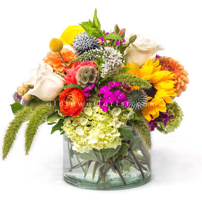 Mixed bouquet in a clear glass vase with sunflowers, roses, and hydrangeas