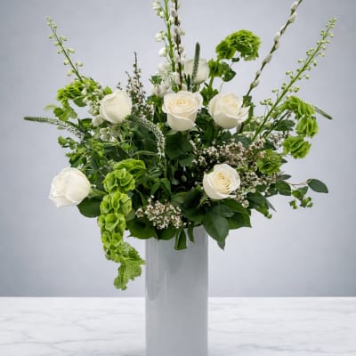 White roses and green blooms arranged in a tall glass vase