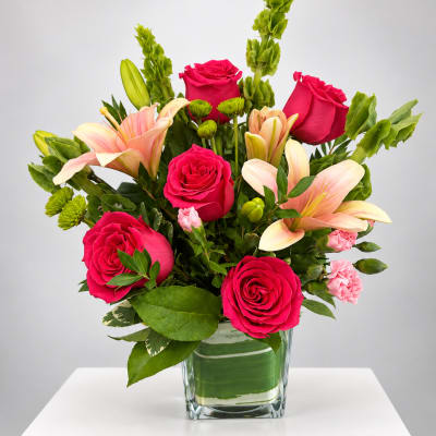 Pink roses and lilies arranged in a clear glass vase