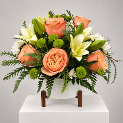 Peach roses and white lilies arranged in a white vase