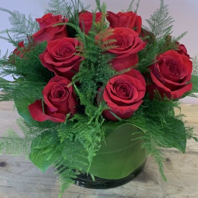 Red roses arranged in a round glass vase with airy greenery