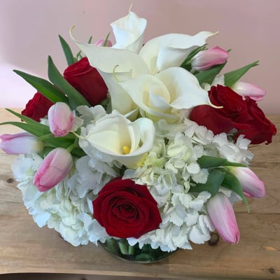 Bouquet of white calla lilies, red roses, and pink tulips in a glass vase