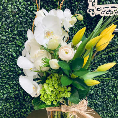 White orchids and yellow tulips in a glass vase with a raffia bow