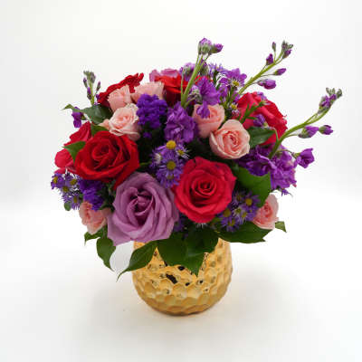 Mixed bouquet of red, pink, and purple roses in a gold vase