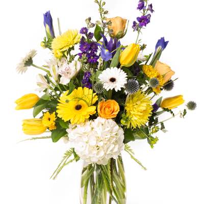 Mixed bouquet of yellow, purple, white, and orange flowers in a clear glass vase