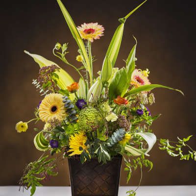 Tall mixed flower arrangement in a dark square vase