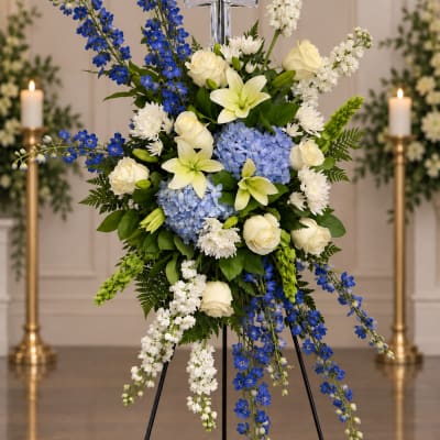 Tall funeral spray with blue and white flowers and a silver cross