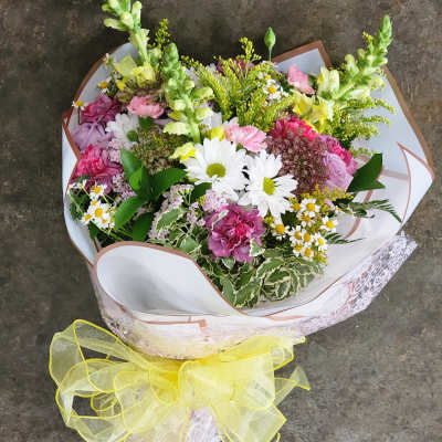 Mixed bouquet of pink, white, and yellow flowers wrapped with a yellow ribbon