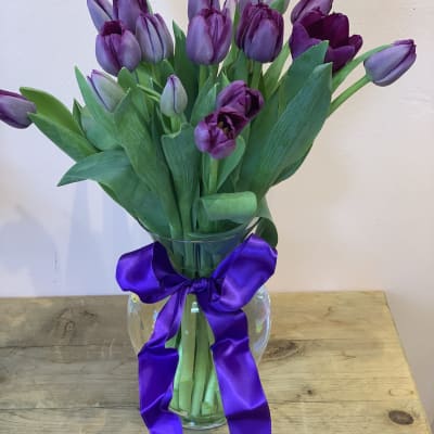 Purple tulips in a clear glass vase with a purple ribbon bow