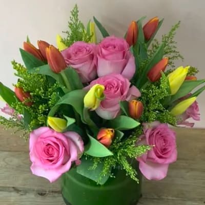 Pink roses and orange-yellow tulips in a green glass vase