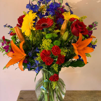 Colorful mixed bouquet in a clear glass vase with lilies, roses, and daisies
