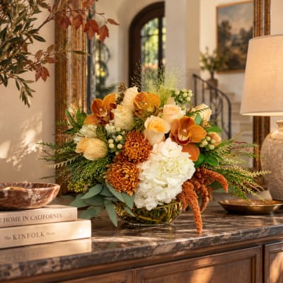 Autumn floral arrangement in a glass bowl with orange, cream, and white blooms