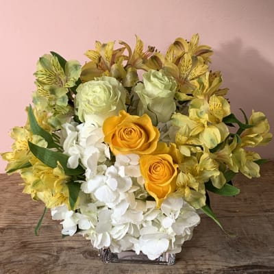 Yellow roses and white hydrangeas in a clear square vase