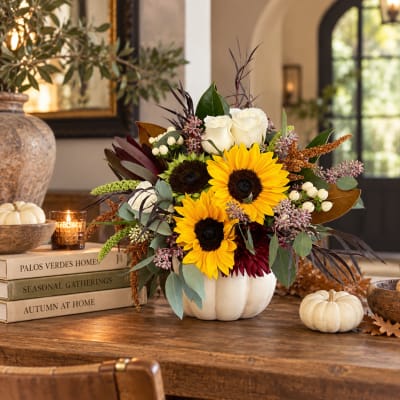 Sunflowers, white roses, and burgundy blooms arranged in a white pumpkin vase