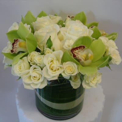 White roses and green orchids arranged in a glass vase
