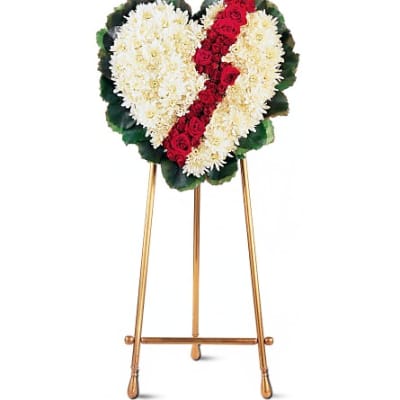 Heart-shaped funeral wreath of white flowers with a red rose stripe on an easel