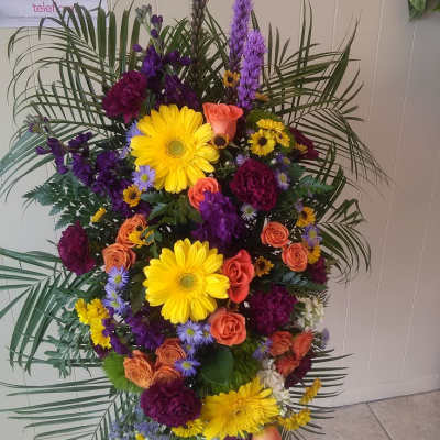 Tall standing floral spray with yellow daisies, orange roses, and purple blooms