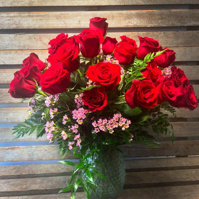 Red roses arranged in a glass vase with pink filler flowers