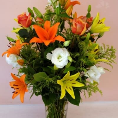 Bouquet of orange and yellow lilies with white blooms in a clear glass vase