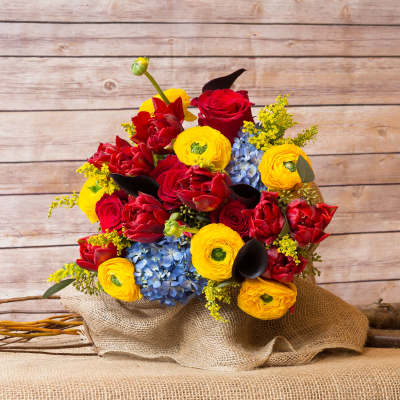 Bouquet of red and yellow flowers with blue blooms wrapped in burlap