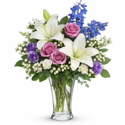 Bouquet of white lilies, pink roses, and blue flowers in a clear glass vase