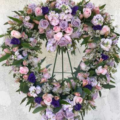 Heart-shaped floral wreath with pink and lavender roses on a stand