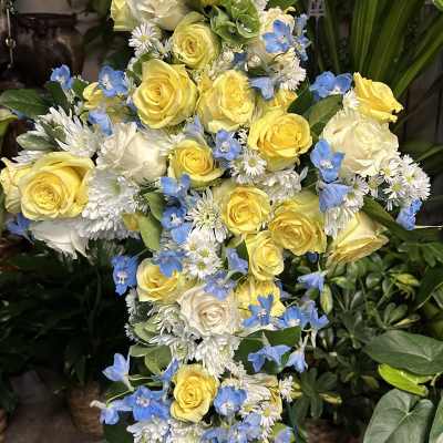 Tall floral spray of yellow and white roses with blue accent flowers