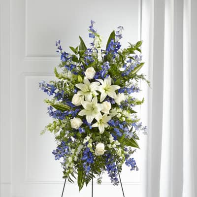 Standing spray of white lilies and roses with blue delphinium on a metal easel