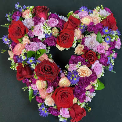 Heart-shaped bouquet of red, pink, and purple flowers on a dark background