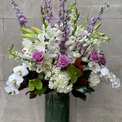 Tall bouquet of white orchids, lilies, hydrangeas, and purple roses in a glass vase
