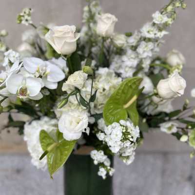 White floral arrangement with roses and orchids in a tall vase