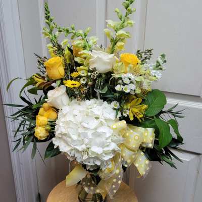 Yellow and white floral arrangement in a glass vase with a ribbon